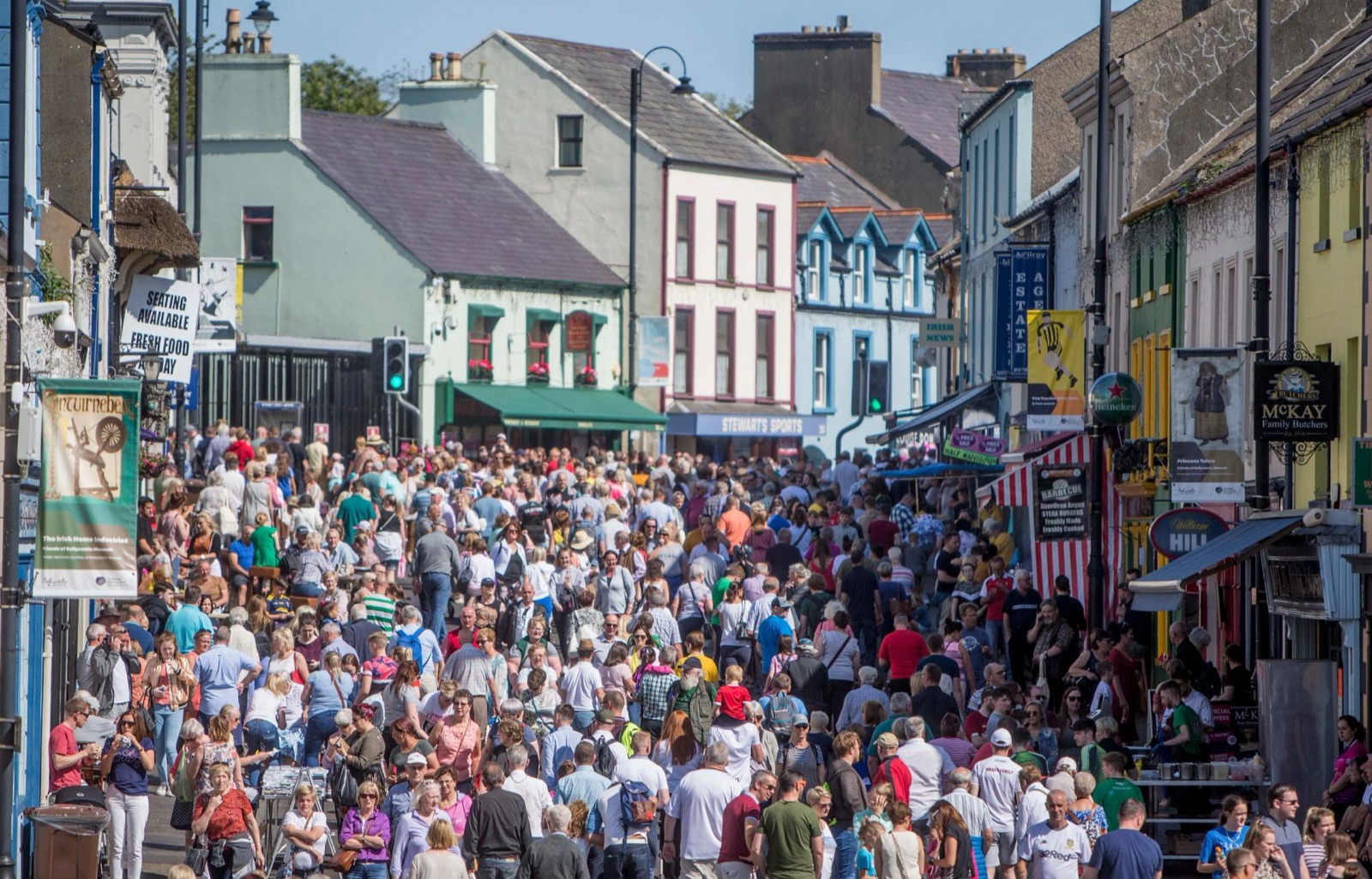 Crowds filling the street of the Ould Lammas Fair between the colourful shopfronts of Ballycastle in the sun