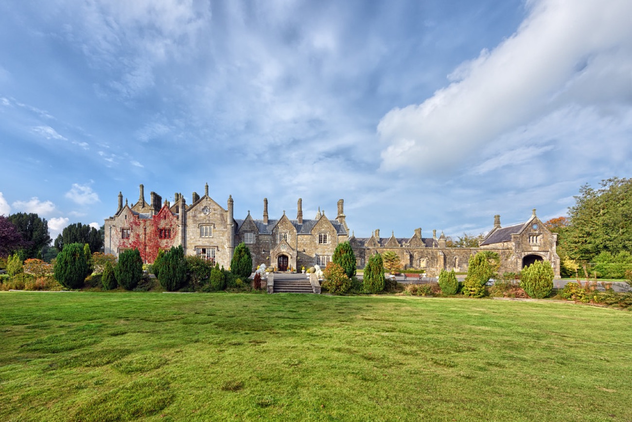 The front of Parkanaur Manor across a broad green lawn, its Gothic gables and chimneys behind clipped topiary and flower beds