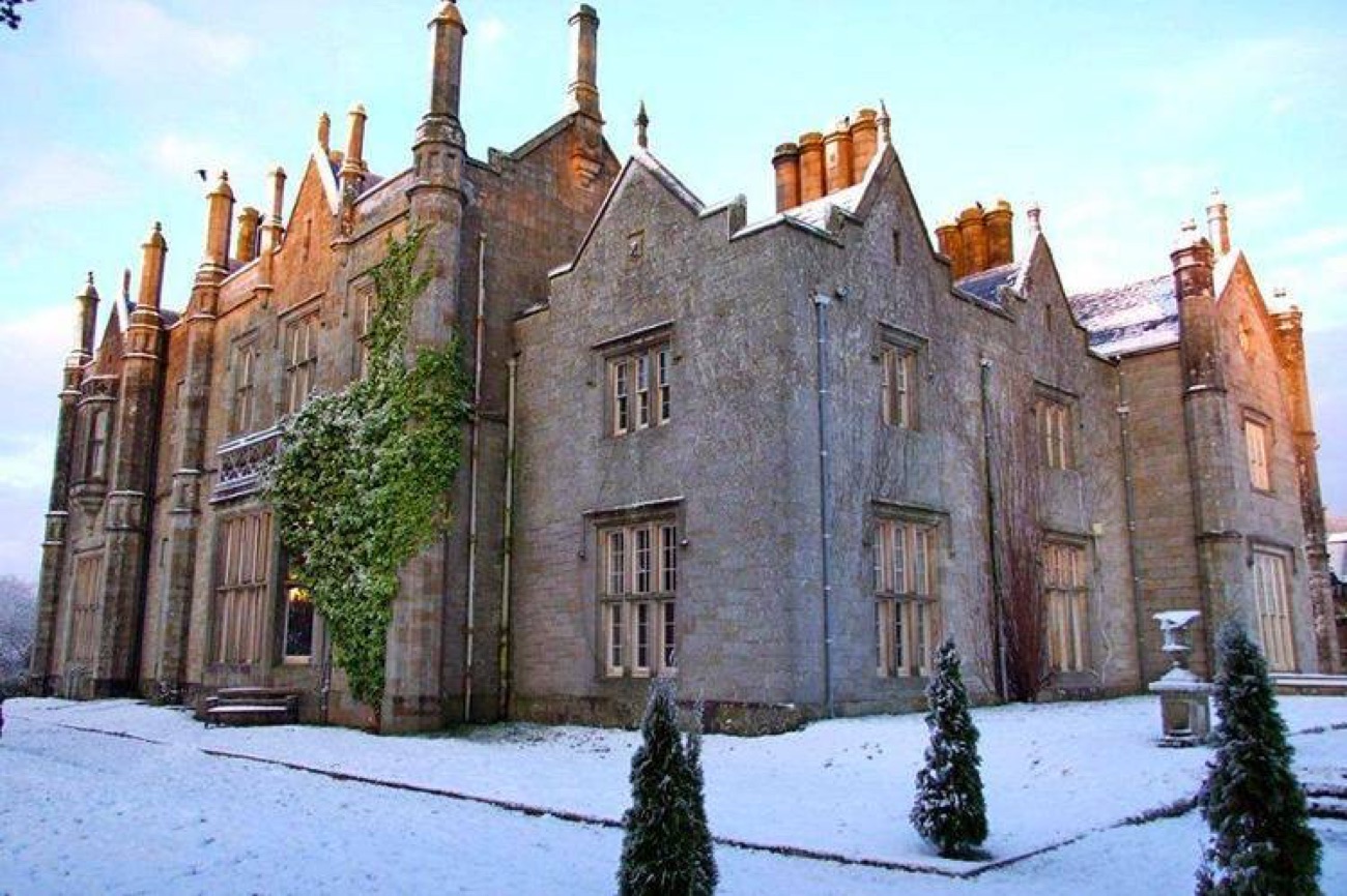 Close view of the grey stone Gothic gables and clustered chimneys of Parkanaur Manor with light snow on the ground