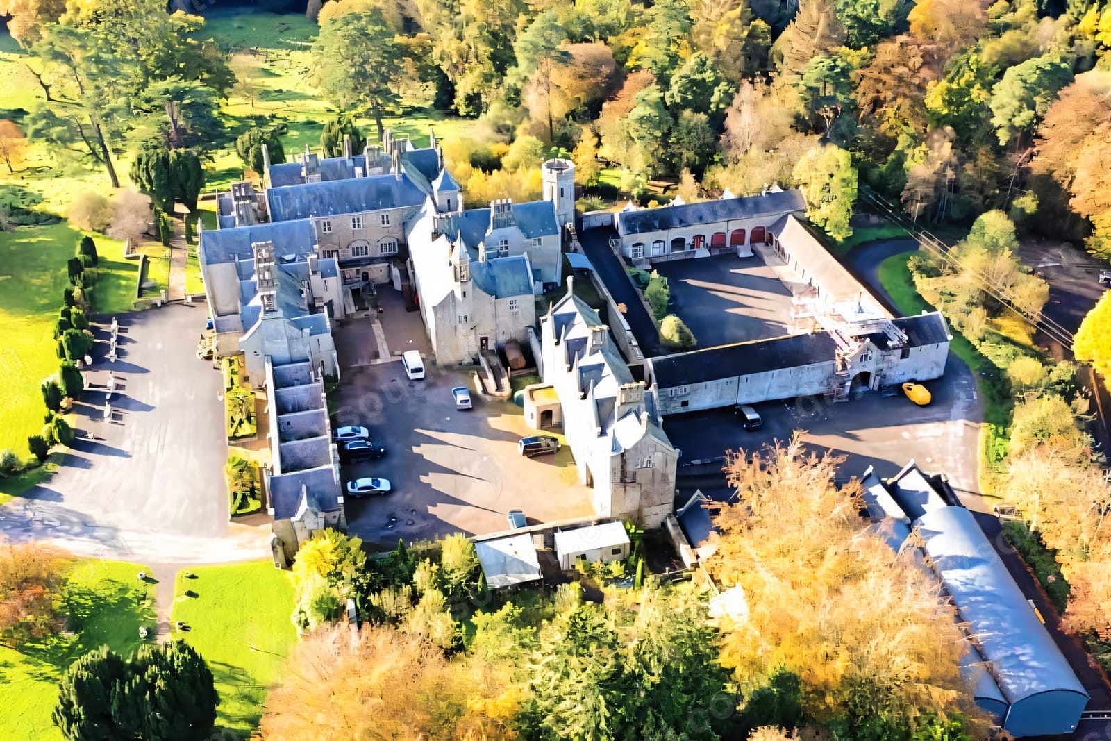 Aerial view of the Gothic-style Parkanaur Manor among autumn woodland, its grey stone wings ringed by mature trees turning gold