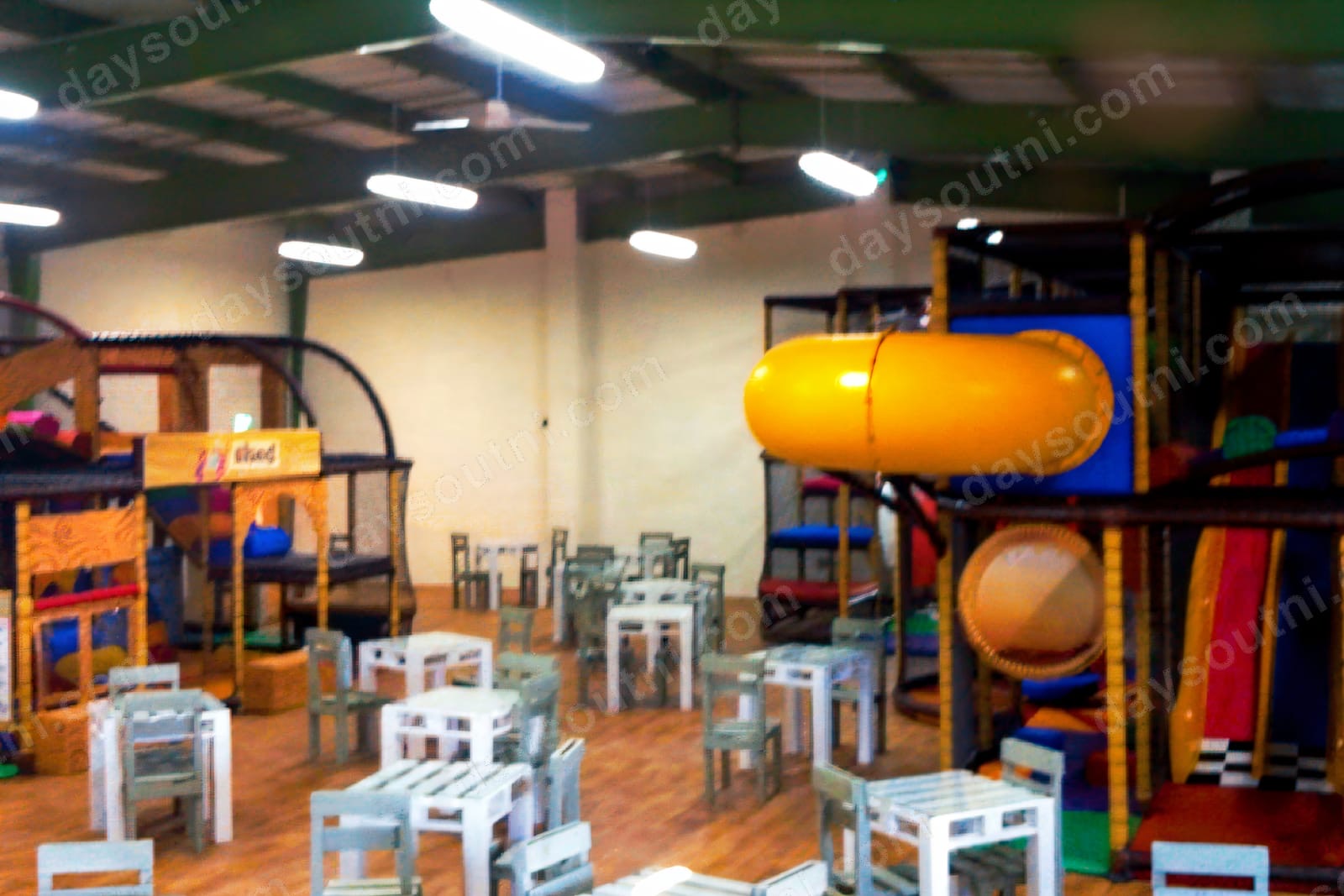 The indoor play frames at The Play Shed, Derry, with a yellow tube slide, climbing frames and café tables in front