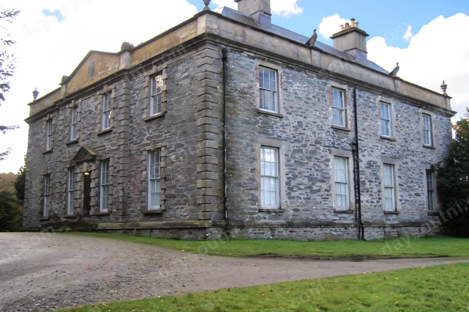 The grey stone Georgian front of Prehen House seen from the corner, with sash windows and a lawn