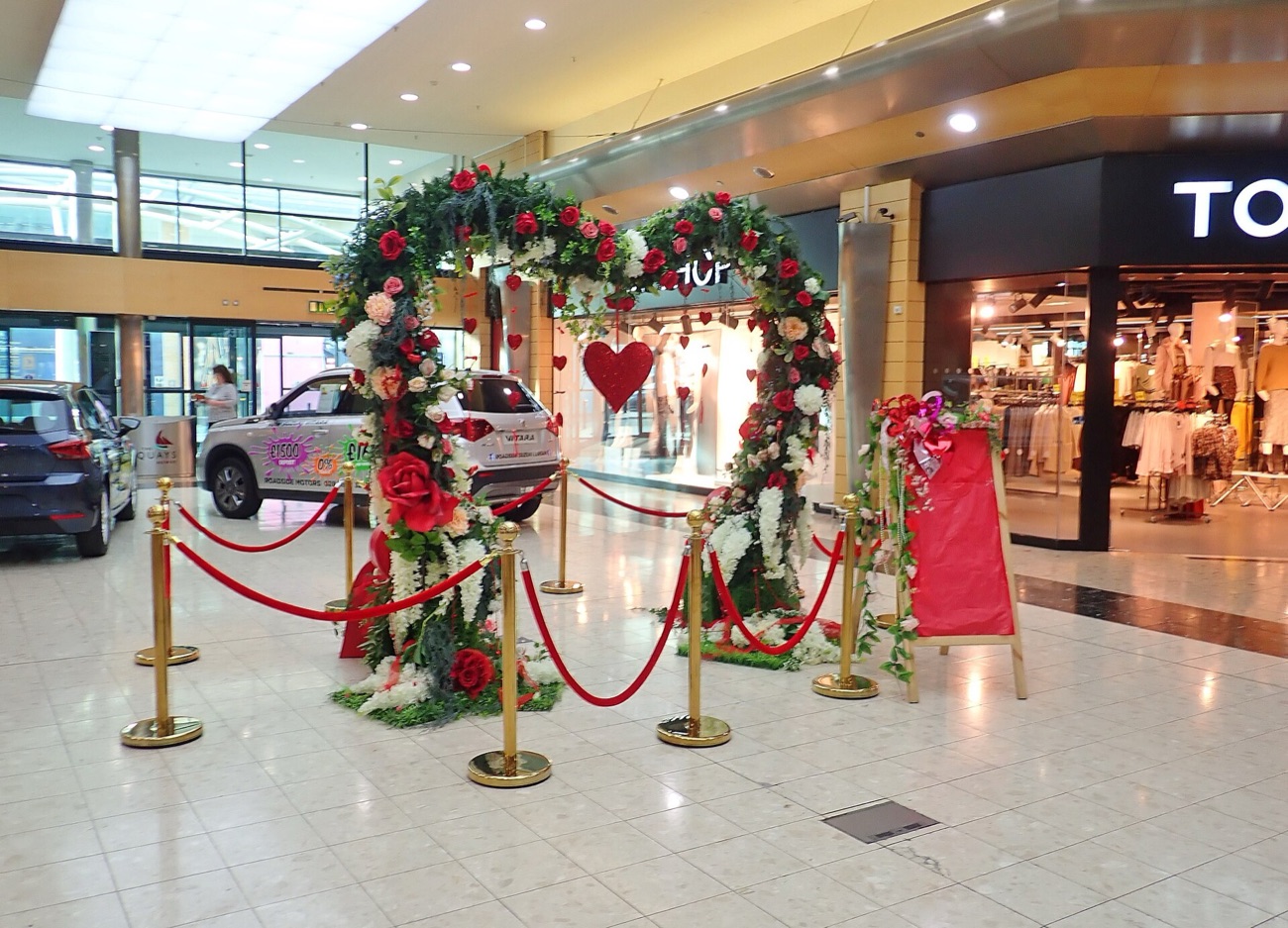 Inside the mall at The Quays, with a floral Valentine's display on the polished concourse and shopfronts either side
