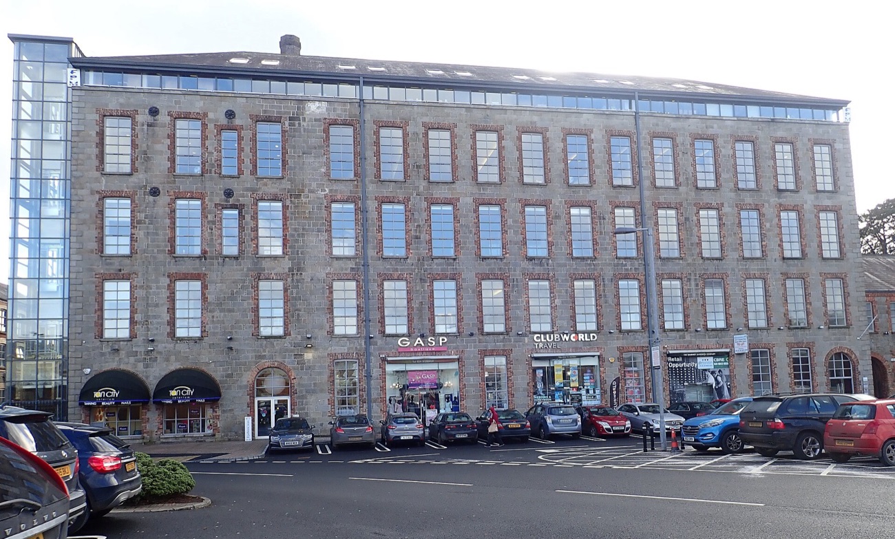 The tall stone face of Drumalane Mill, the old mill building folded into The Quays complex, with shop units at street level