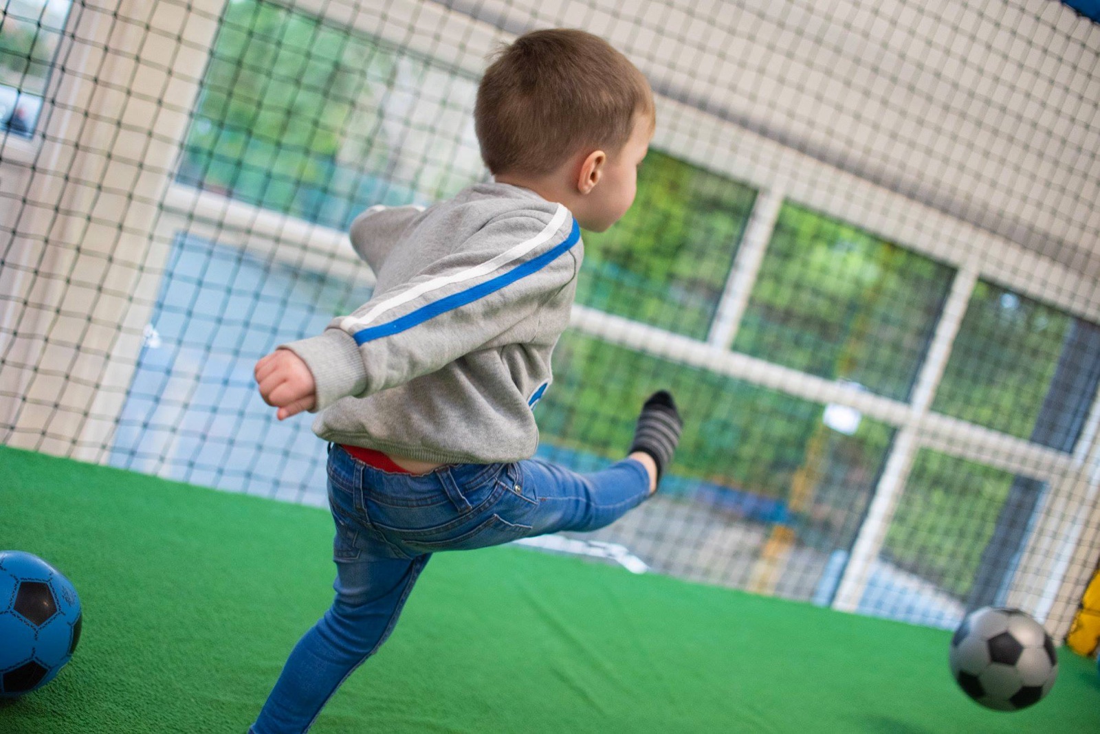 A child kicking a ball on the indoor football court at Rascalz soft play in Castlederg, with netting and green astroturf