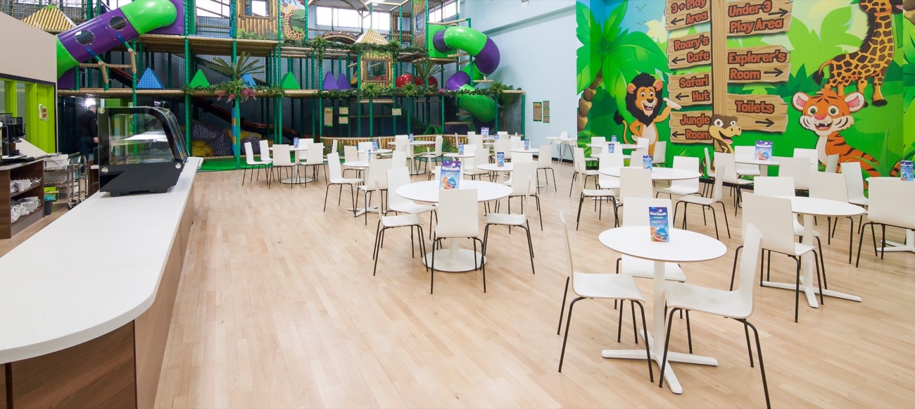Roary's Café at Roar and Explore, with white tables and chairs, the jungle play frame behind and a lion-and-tiger mural with area signage