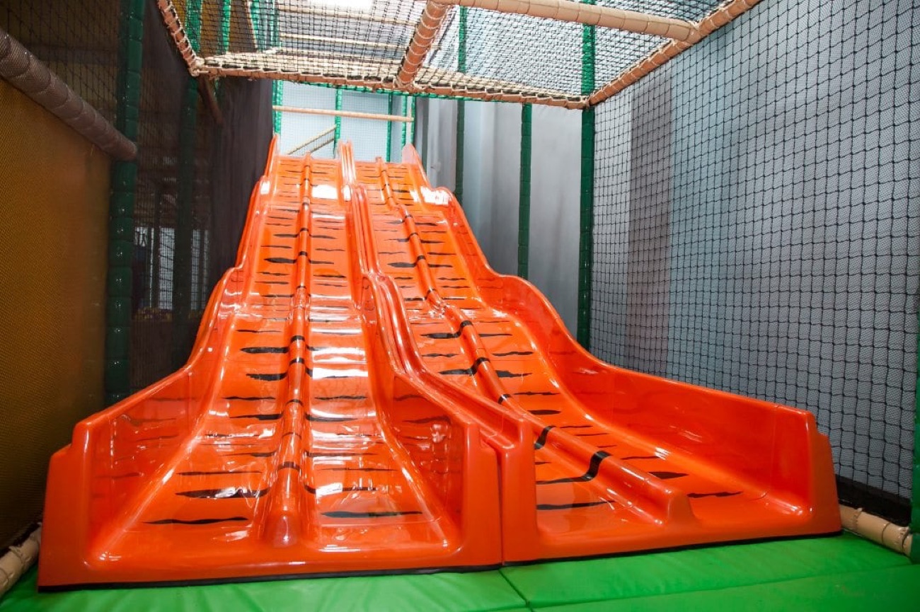 A wide orange double slide inside the Roar and Explore soft play frame