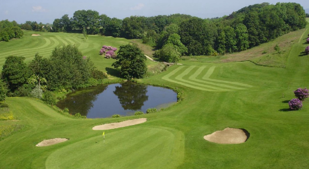 A parkland golf hole with a pond, bunkers and a flag on the green
