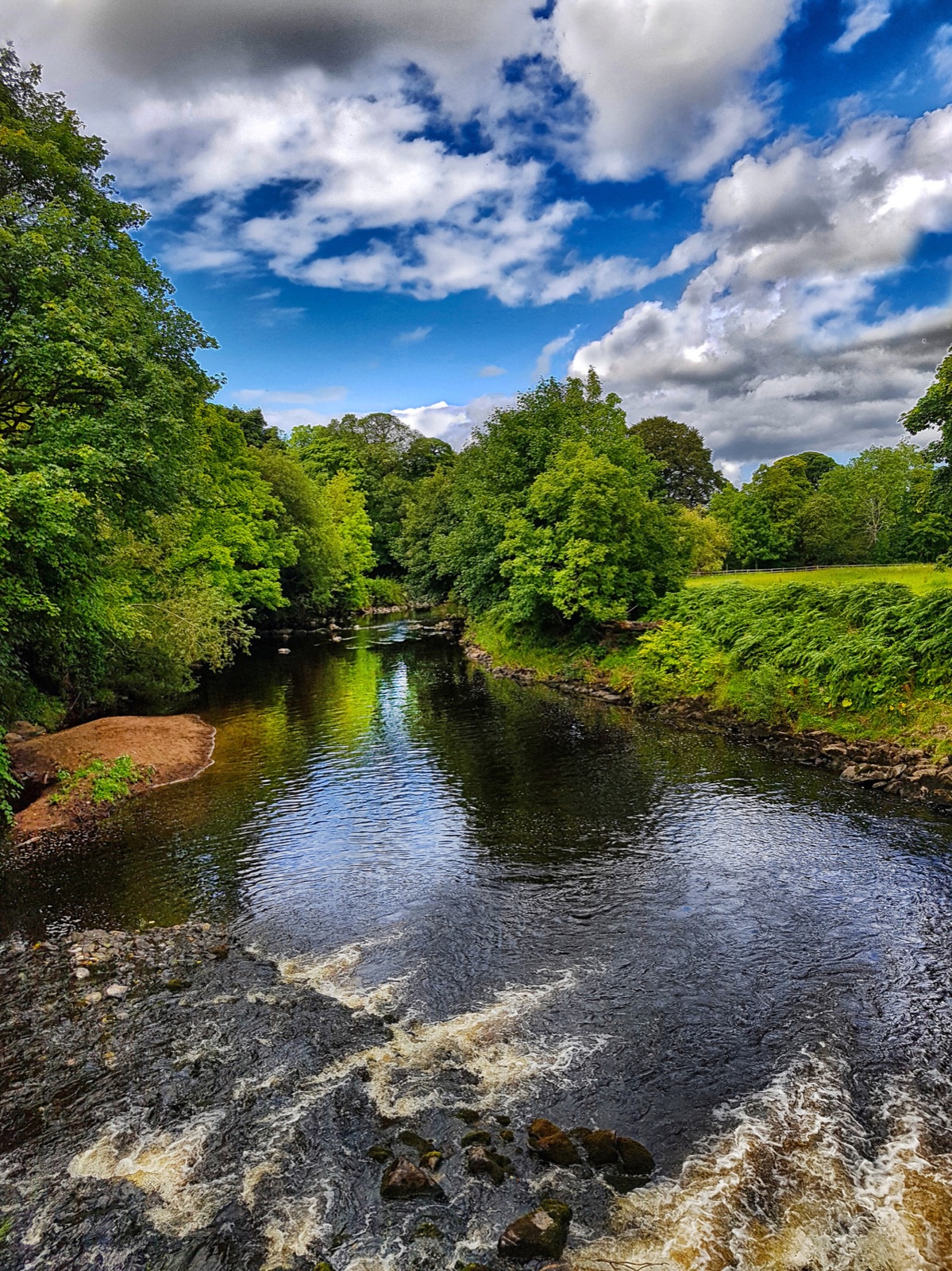 The River Roe winds between lush green banks with white water tumbling over the rocks.