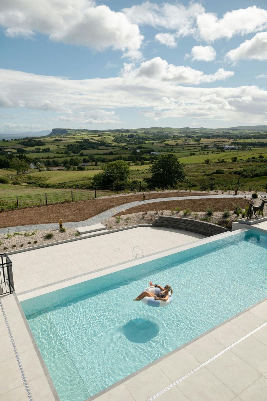 The heated outdoor infinity pool set above a patchwork of green Antrim fields running down to the sea.