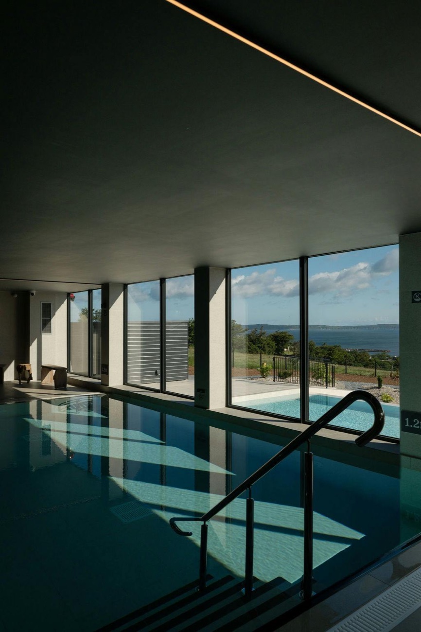 The indoor vitality pool with floor-to-ceiling windows opening onto the coast.