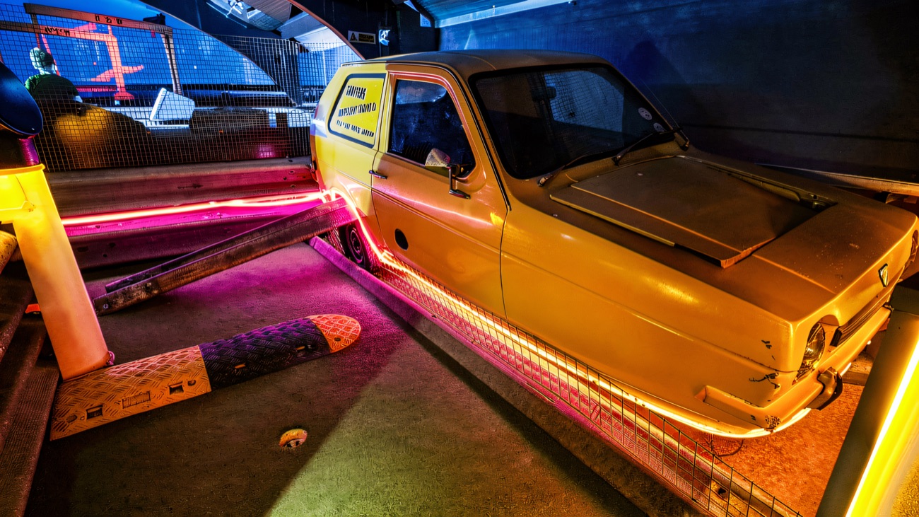 A yellow three-wheeled van built into the neon-lit mini golf course