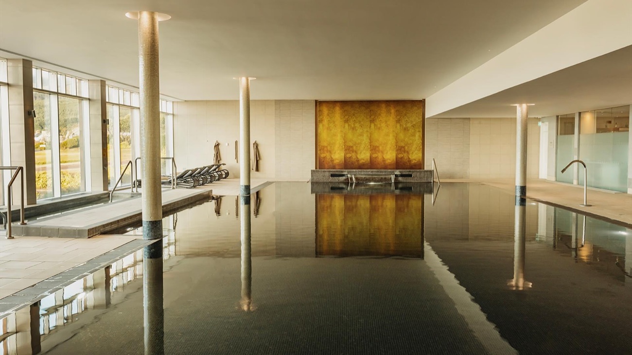 The still indoor pool with a warm gold feature wall and a wall of glass to one side.