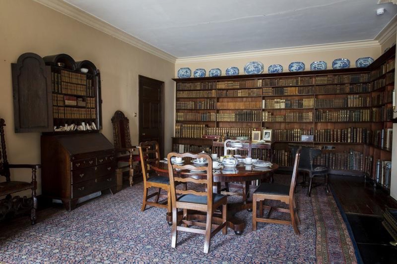 A wood-panelled room inside Springhill lined with shelves of leather-bound books and a round table set with blue-and-white china