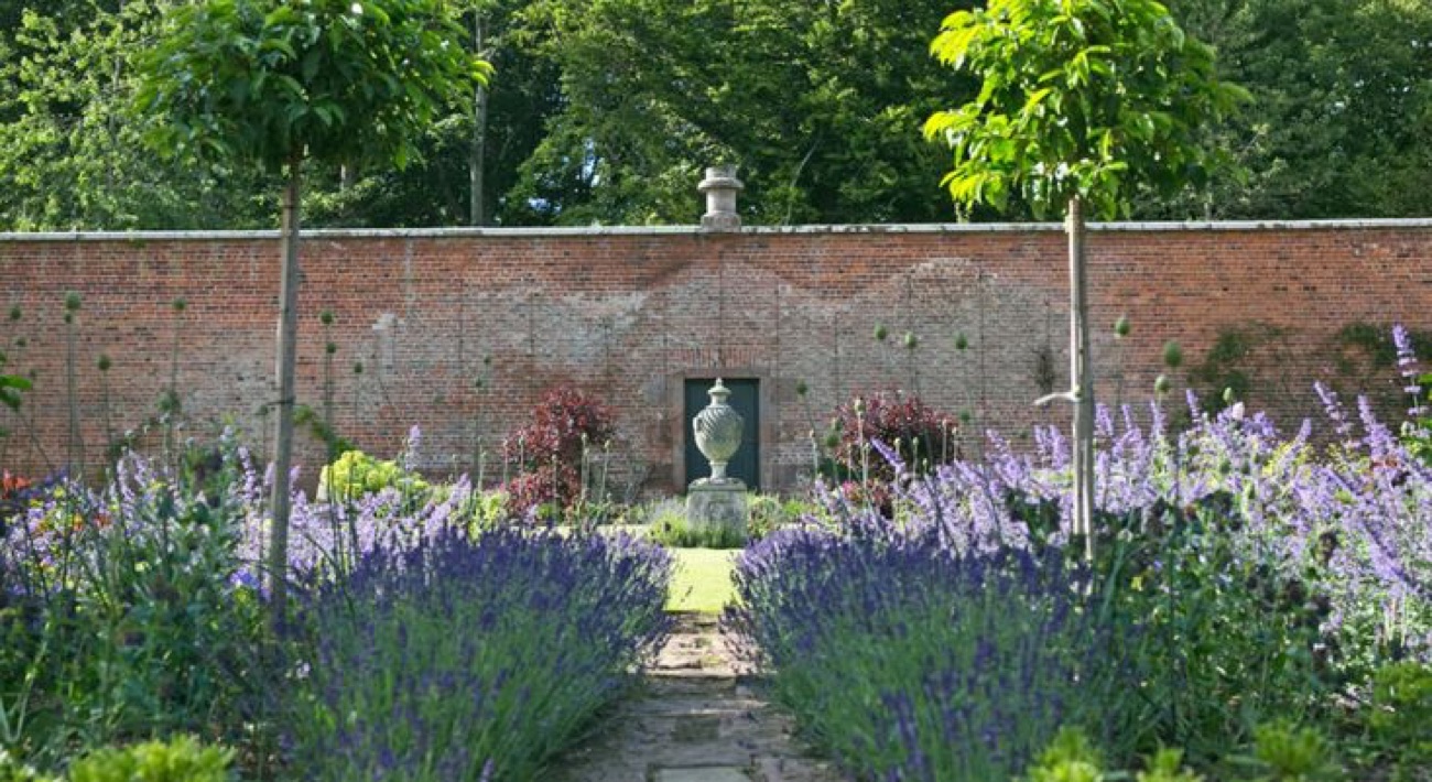A lavender-lined path in the walled garden leading to a stone urn against an old red-brick wall