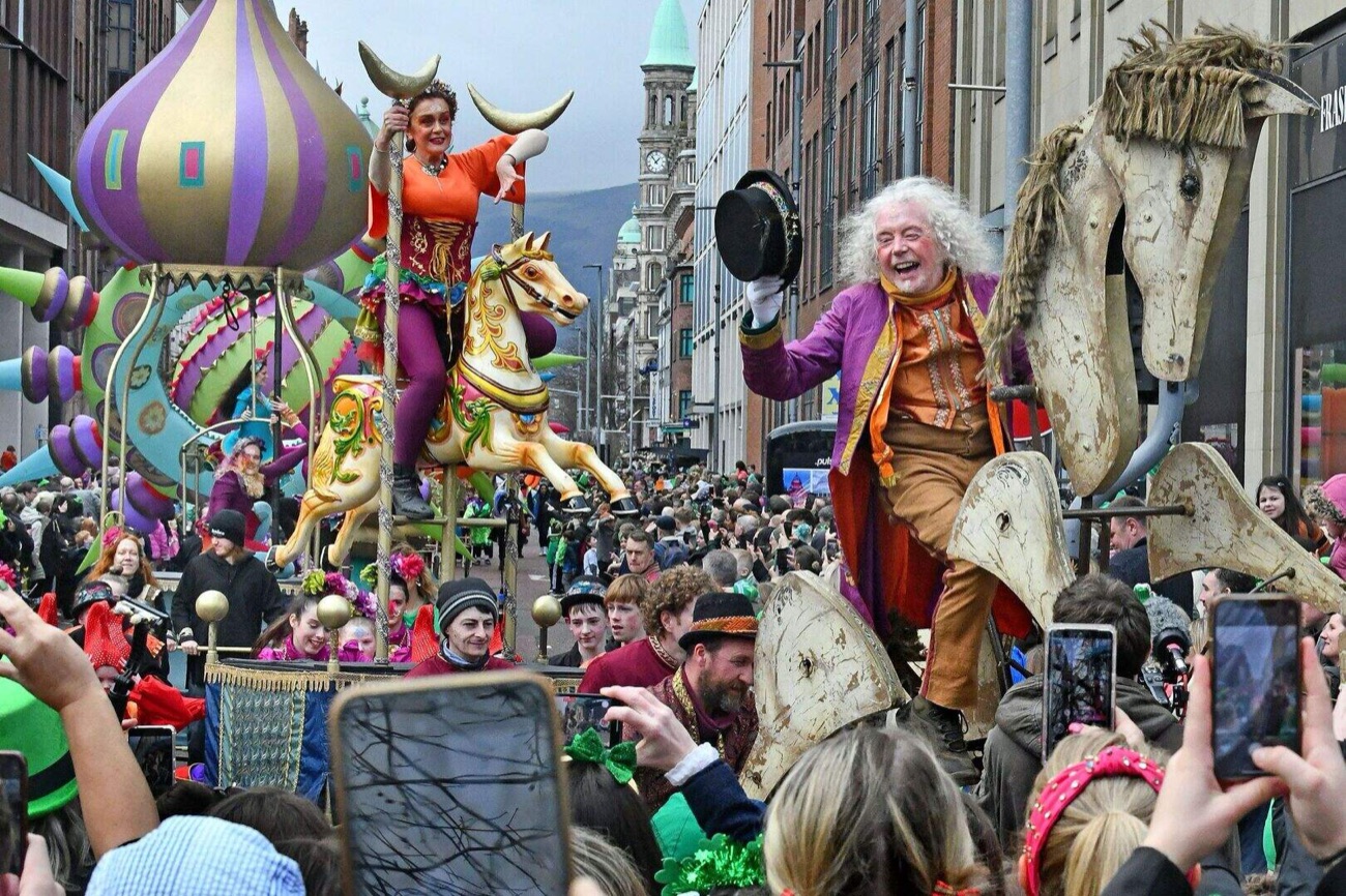 Bright carnival floats and giant puppets moving through crowds at the Belfast St Patrick's Day parade