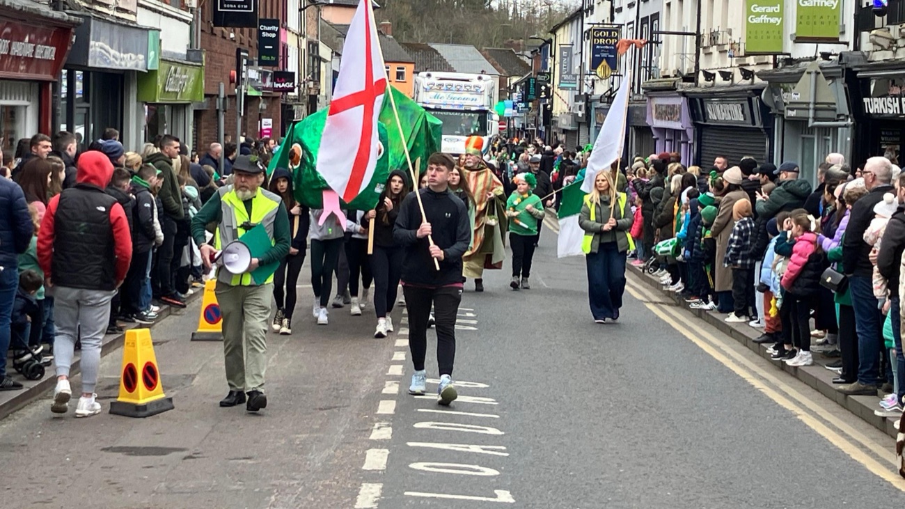 A town St Patrick's Day parade led by the yellow-and-red flag of St Patrick with a green dragon puppet behind
