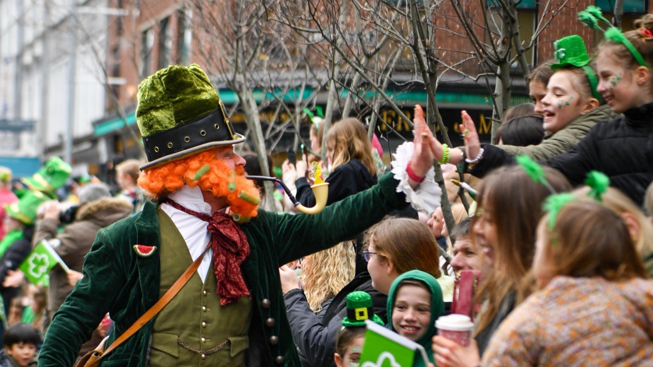 A performer in a green leprechaun costume high-fiving families dressed in green along the parade route