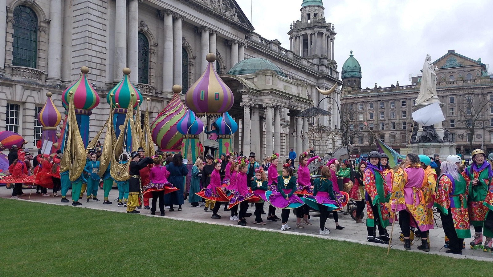 Colourful carnival performers with giant onion-dome puppets on the lawn in front of Belfast City Hall on St Patrick's Day