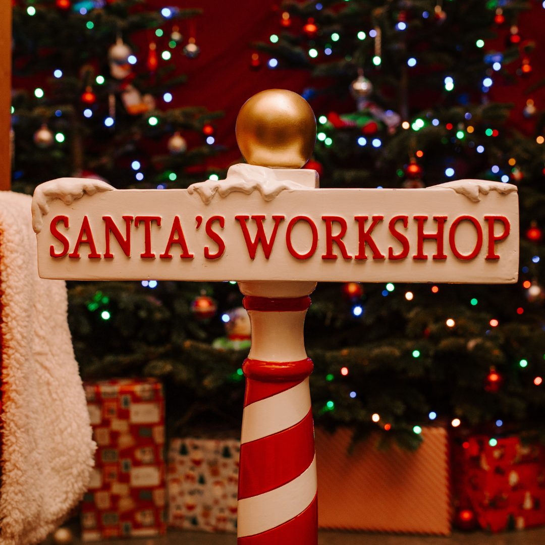 A festive Santa's Workshop sign beside a decorated Christmas tree and wrapped gifts