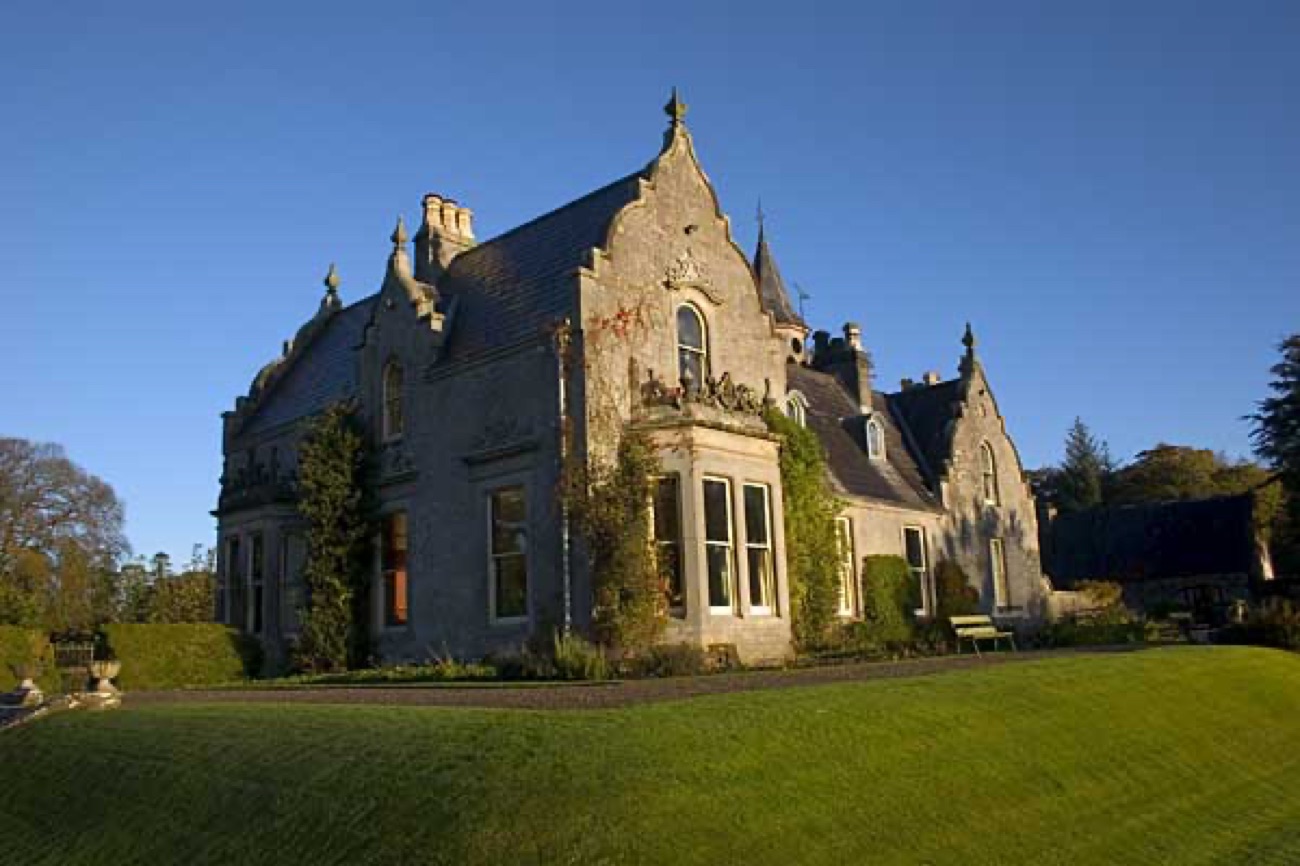 Tempo Manor's grey stone Victorian-Jacobean front lit by low golden sun under a clear sky