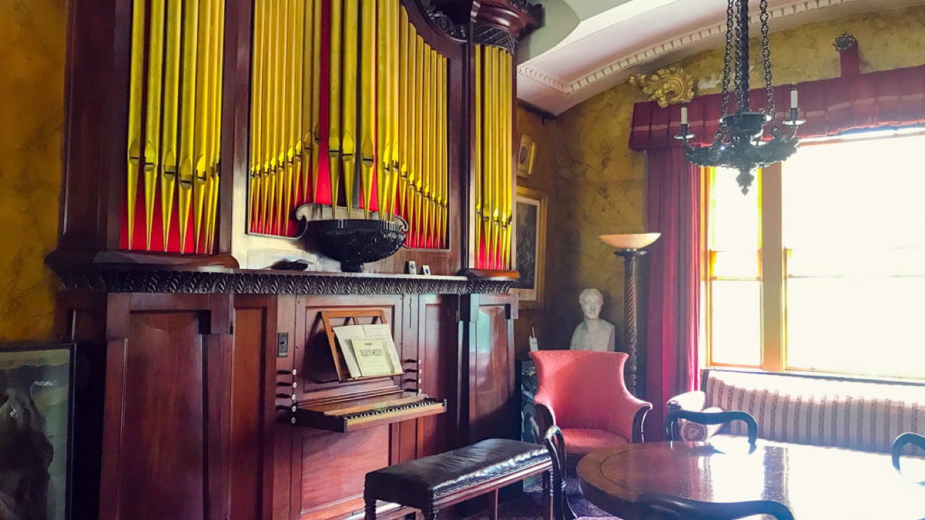 The tall barrel organ with its red and gold pipes standing in a richly furnished drawing room inside The Argory