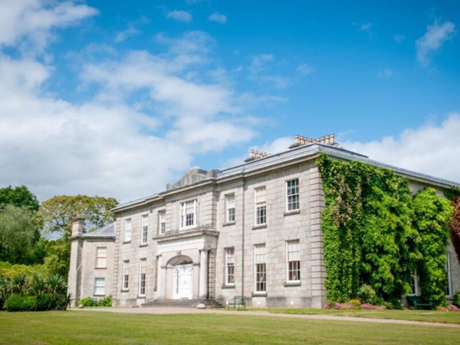 The grey stone Victorian house at The Argory, one wing draped in ivy, seen across a wide green lawn under a blue sky