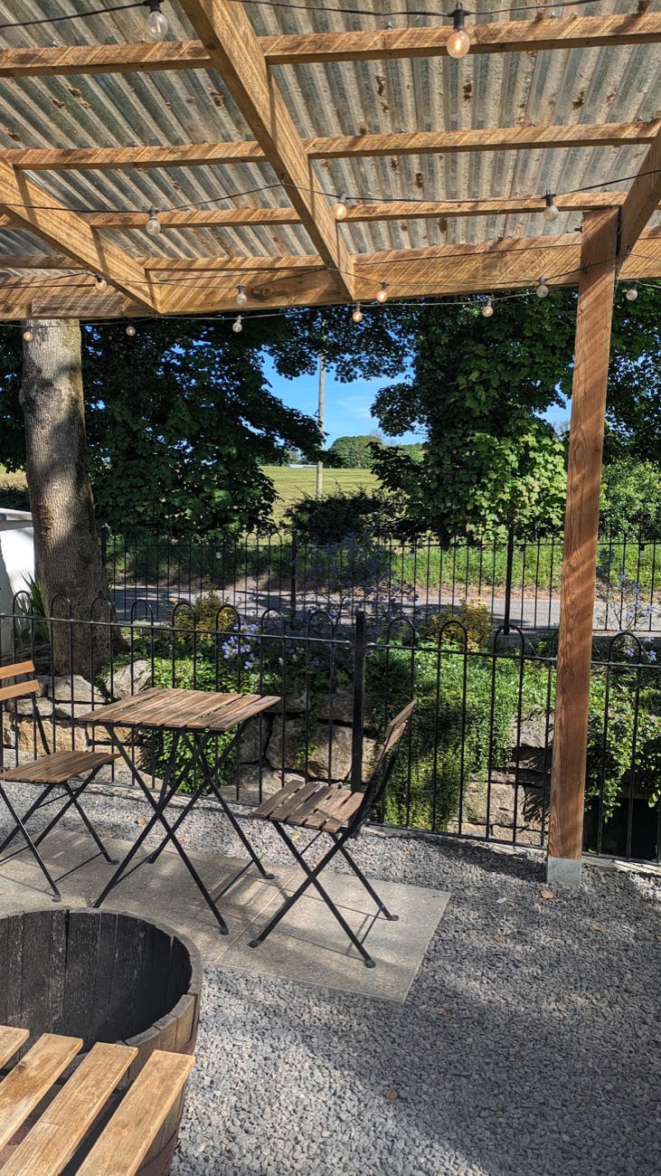 Outdoor tables under a timber pergola at The Croft, looking out over railings to the fields