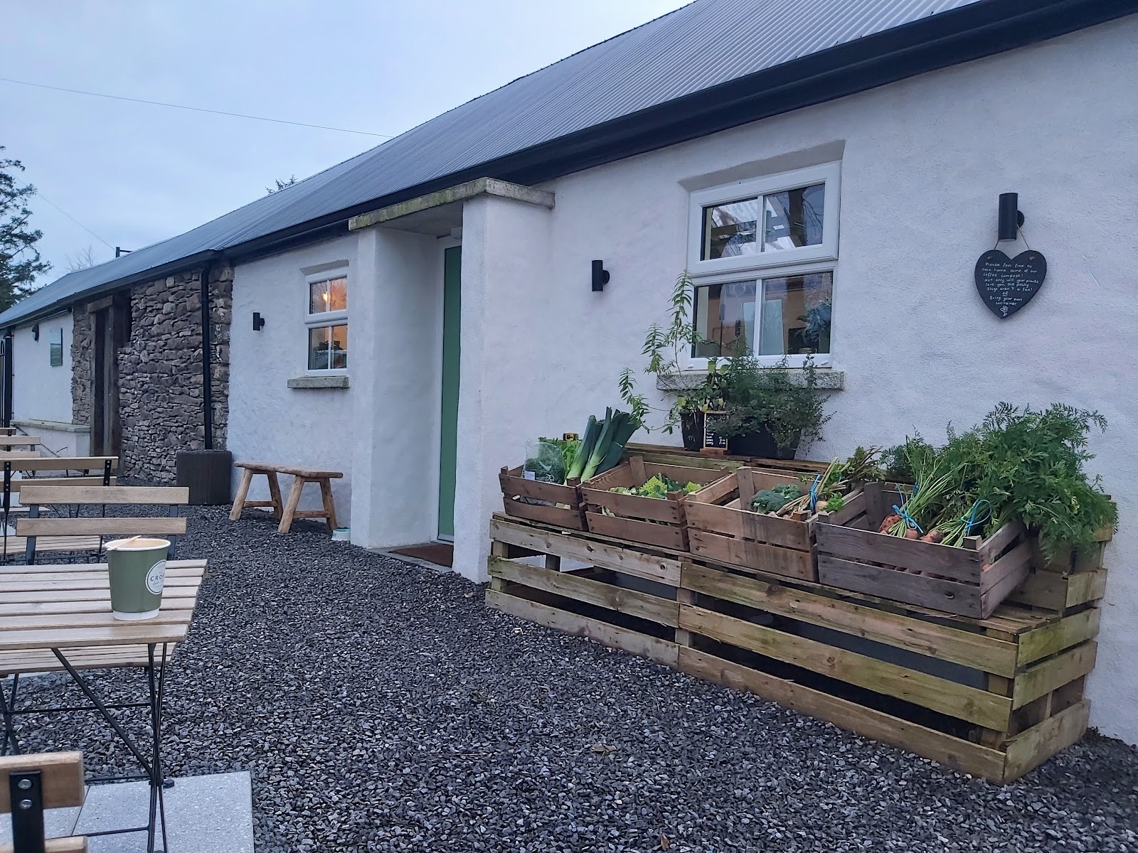The whitewashed Croft Farm Shop with wooden crates of vegetables outside and garden seating on the gravel