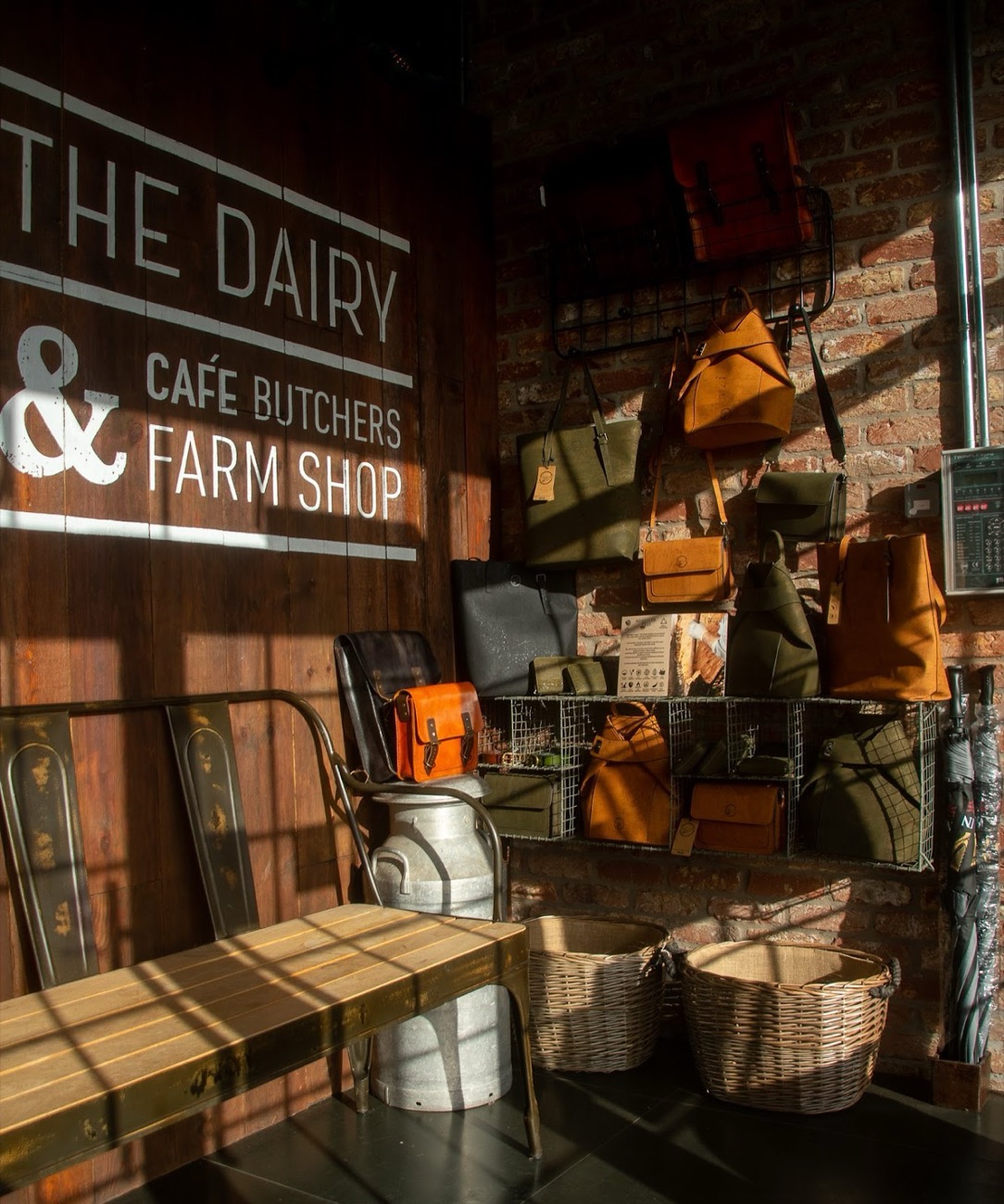 Inside The Dairy: brick and timber wall lettered Café, Butchers, Farm Shop, with leather bags and an old milk churn