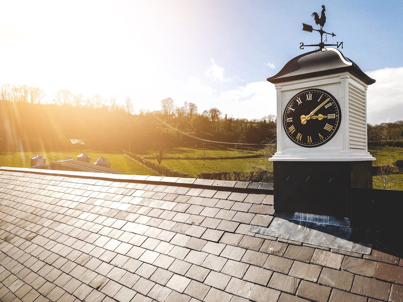 The clock cupola and weathervane against a low sun over the fields of the Gleno valley