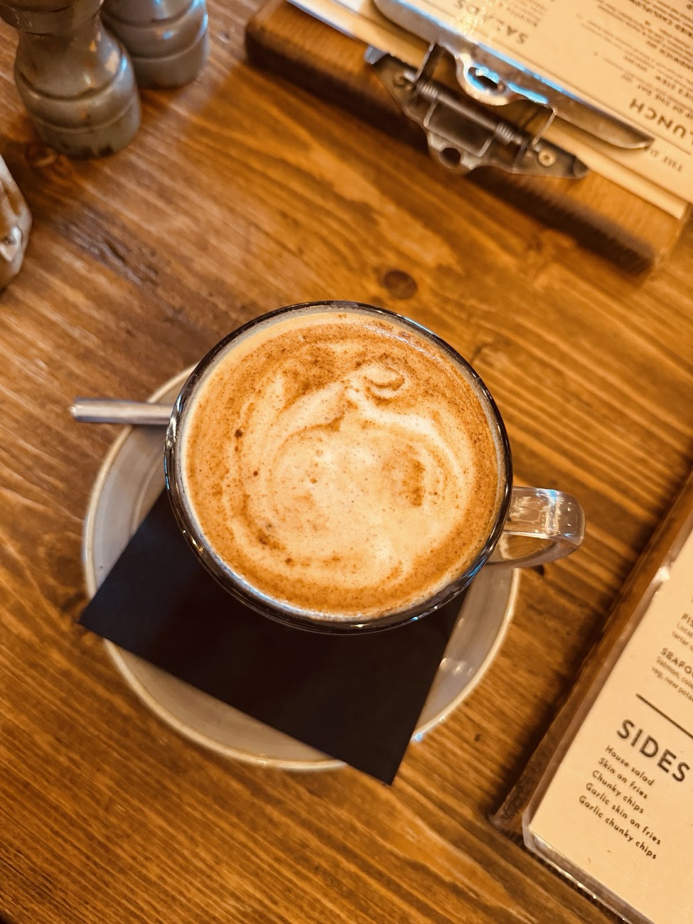 A cappuccino on a scrubbed wooden table beside the menu