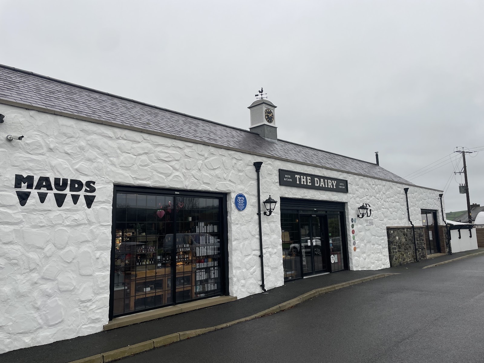 The Dairy at Gleno — a long whitewashed building with a clock cupola and weathervane, the sign reading Bistro, Butchers, Coffee, Farm Shop