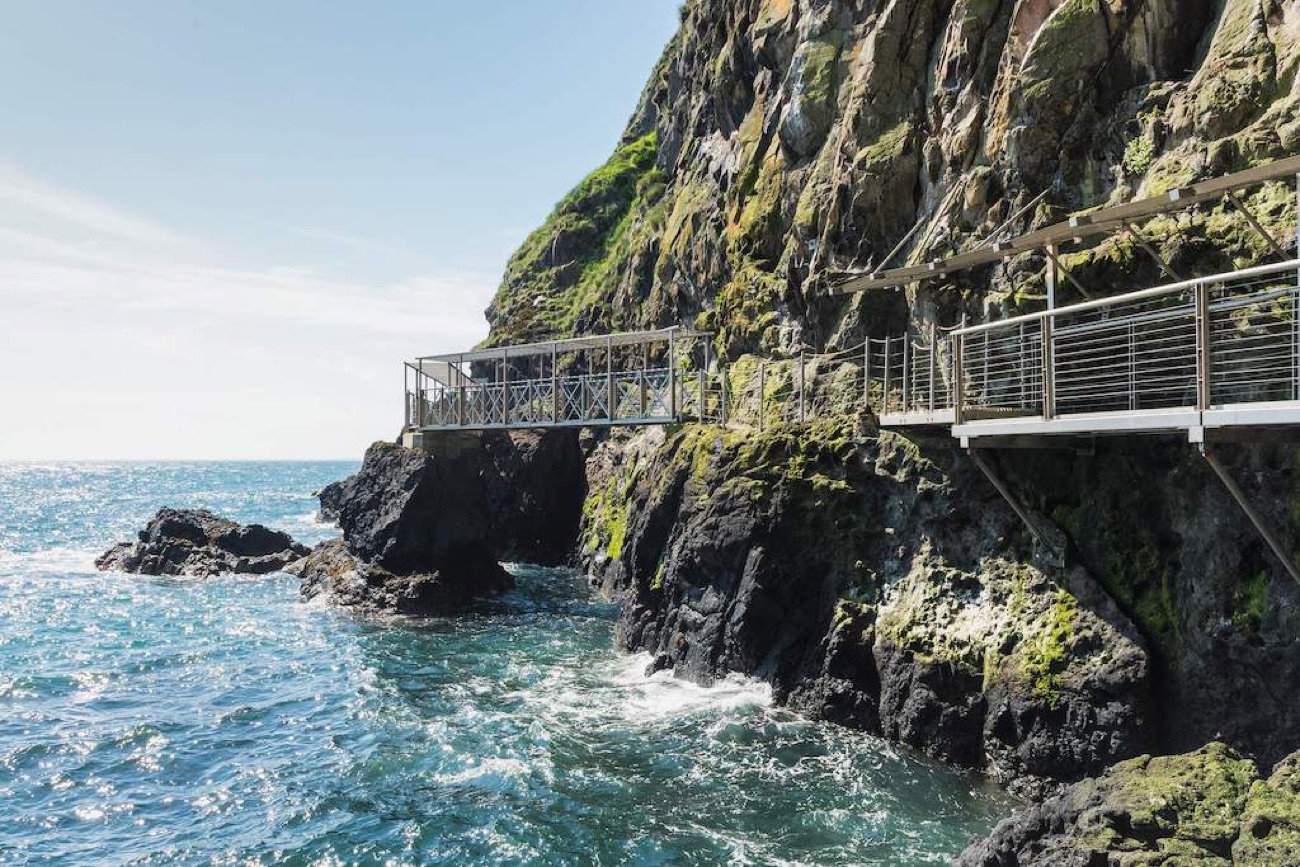 A viewing platform on The Gobbins jutting over turquoise water in bright sun