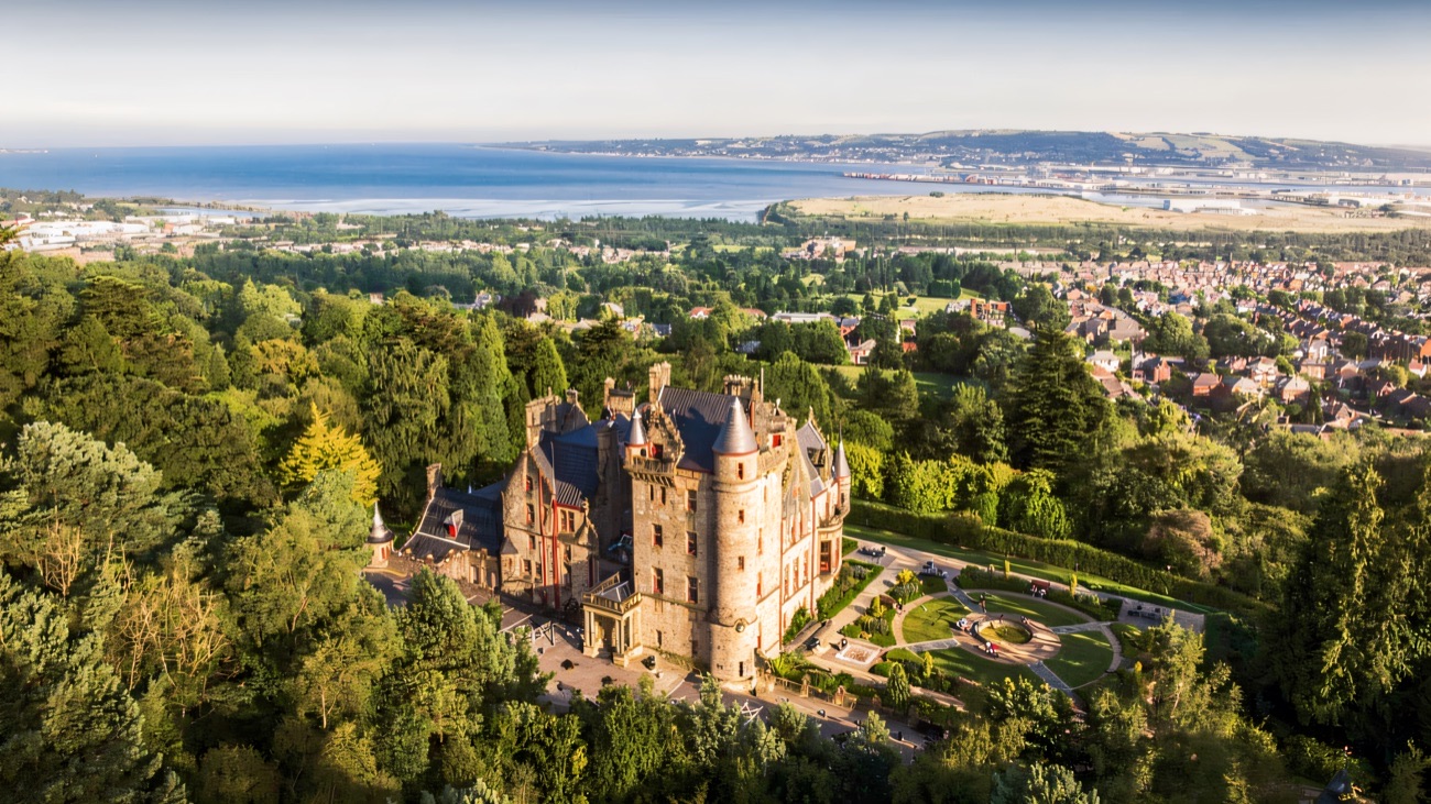 Aerial view of Belfast Castle in its gardens on Cave Hill with Belfast Lough beyond
