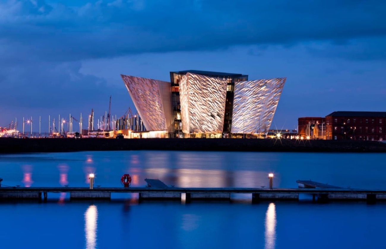 The Titanic Belfast building lit up at dusk, reflected in the water