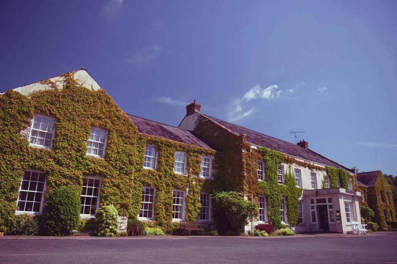 The ivy-covered stone front of Tullylagan Country House against a deep blue sky, with the main entrance below