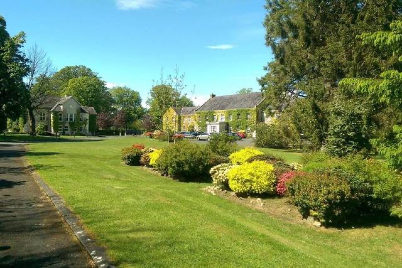 Flowering shrub borders and a manicured green lawn in the gardens at Tullylagan, with the house behind