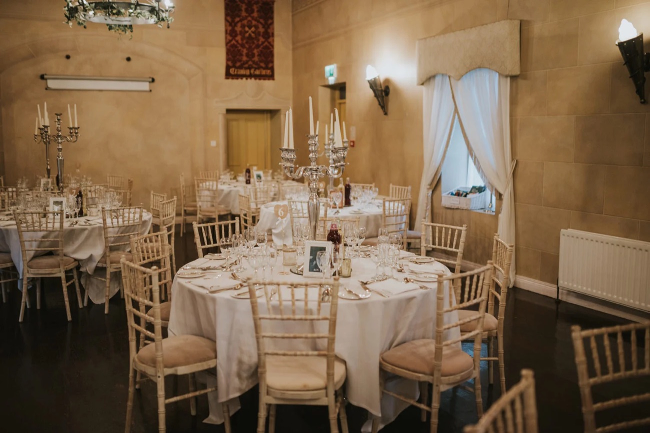 A stone-walled dining room at Tullylagan laid with round tables, white linen and candelabra for an event