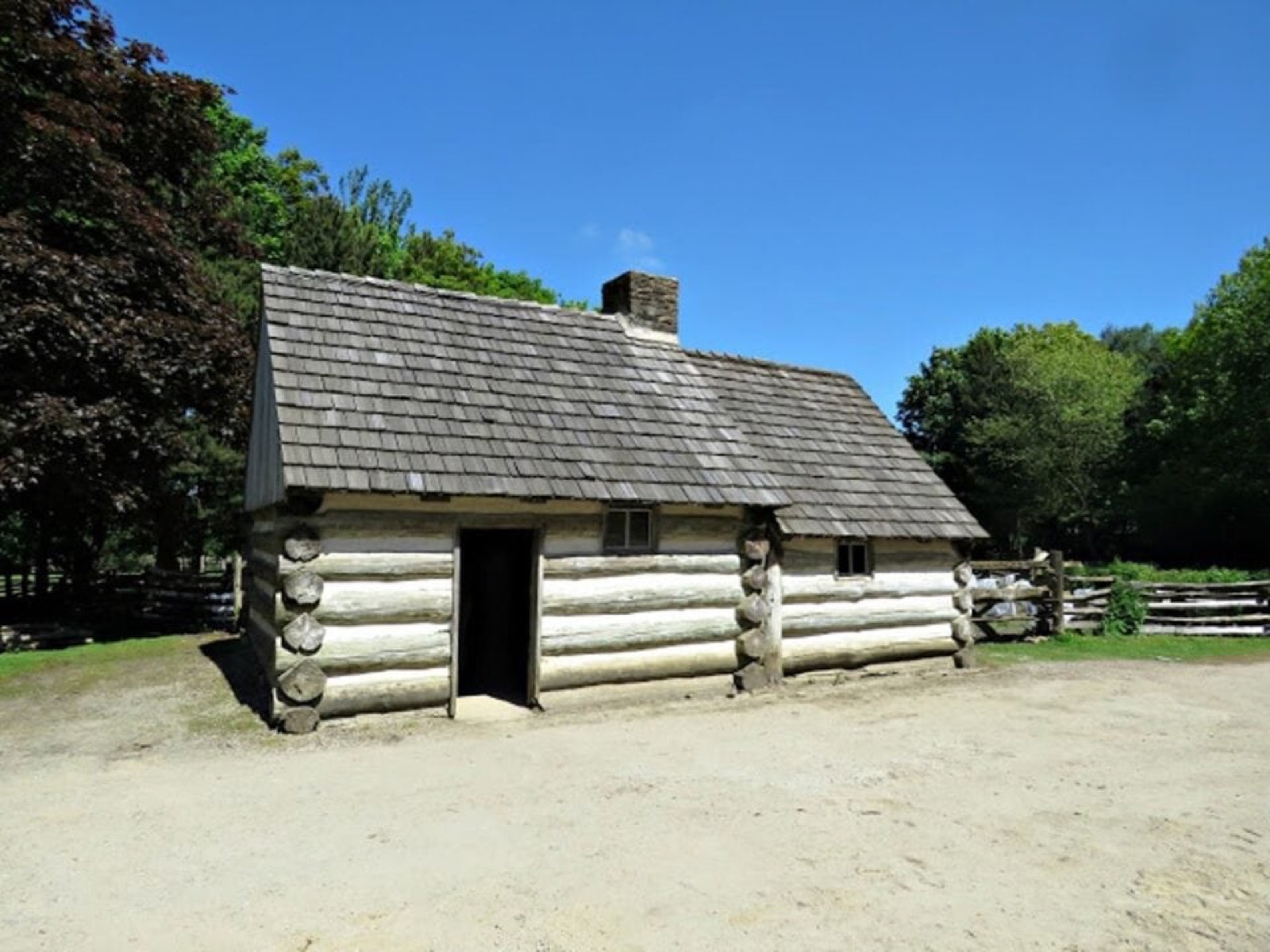A whitewashed log emigrant-era cabin with a shingle roof under a blue sky