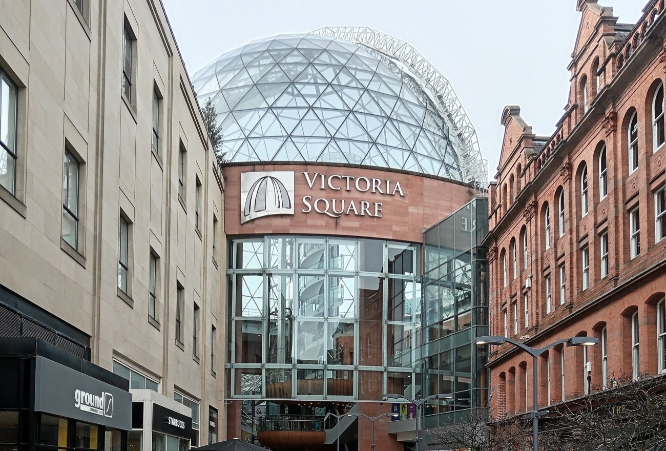 The glass dome of Victoria Square rising above the Victoria Square sign and the red-brick buildings at the entrance from the street