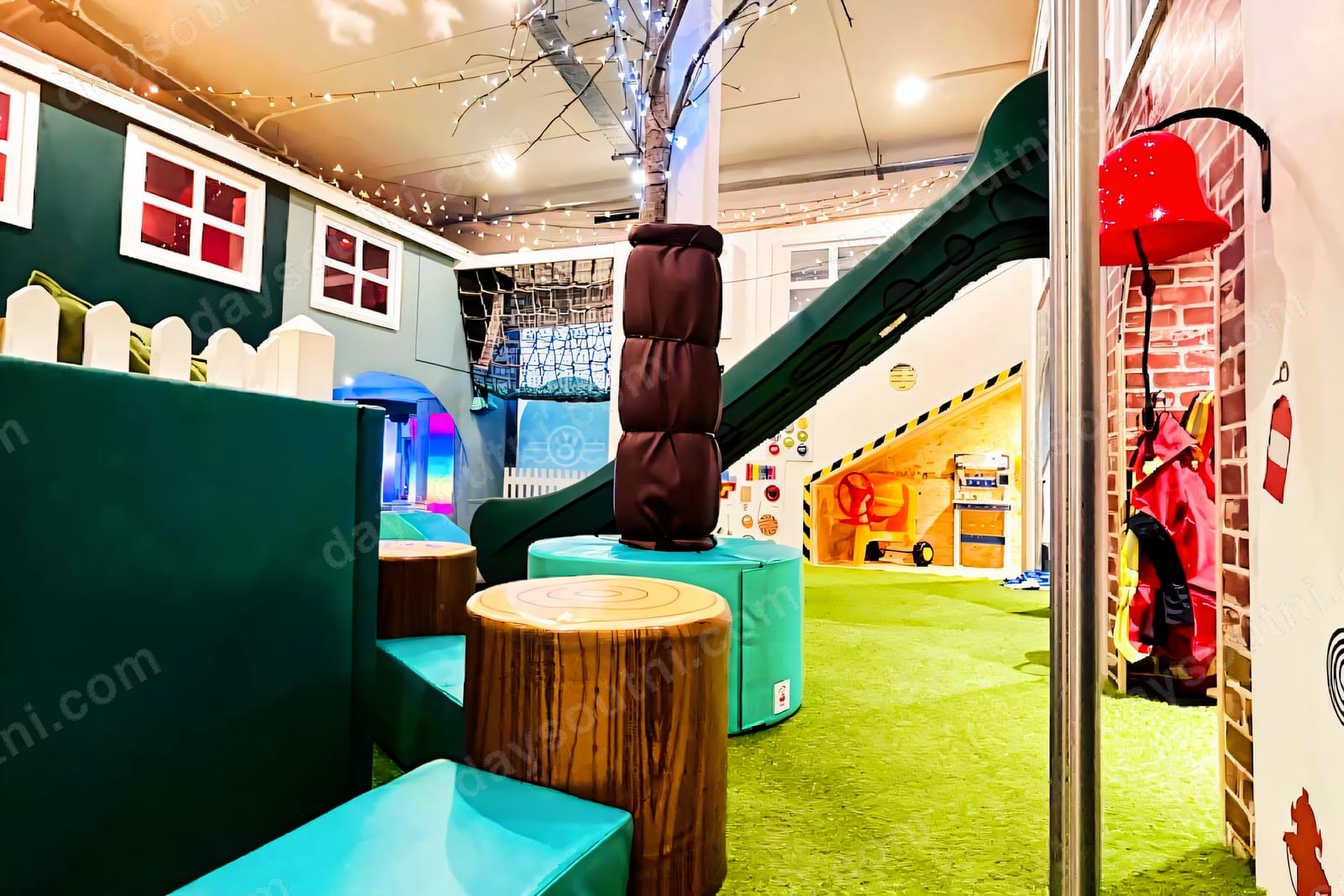 The nature-themed indoor play area at Wee Adventurers Cookstown, with fairy lights, a play tree, a green slide, a fire-station role-play corner and astroturf