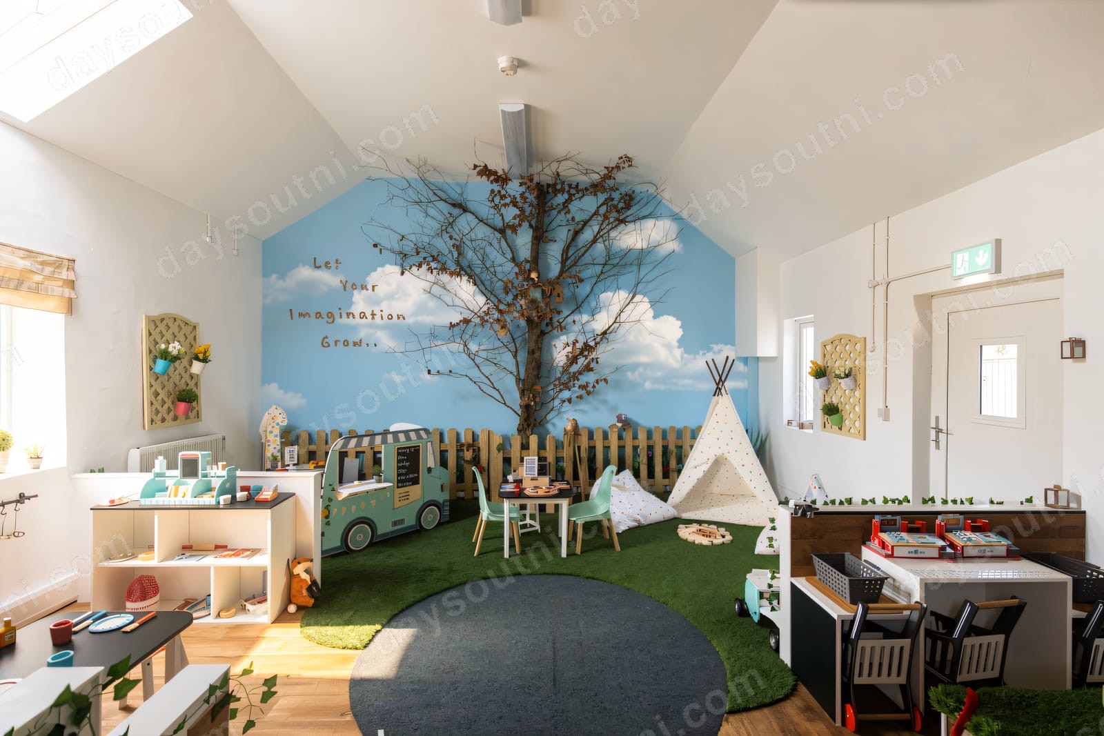 The hand-painted role-play village at The Wee Village near Ballyclare, with a painted tree, teepee, market stalls and a play car under a country-sky mural