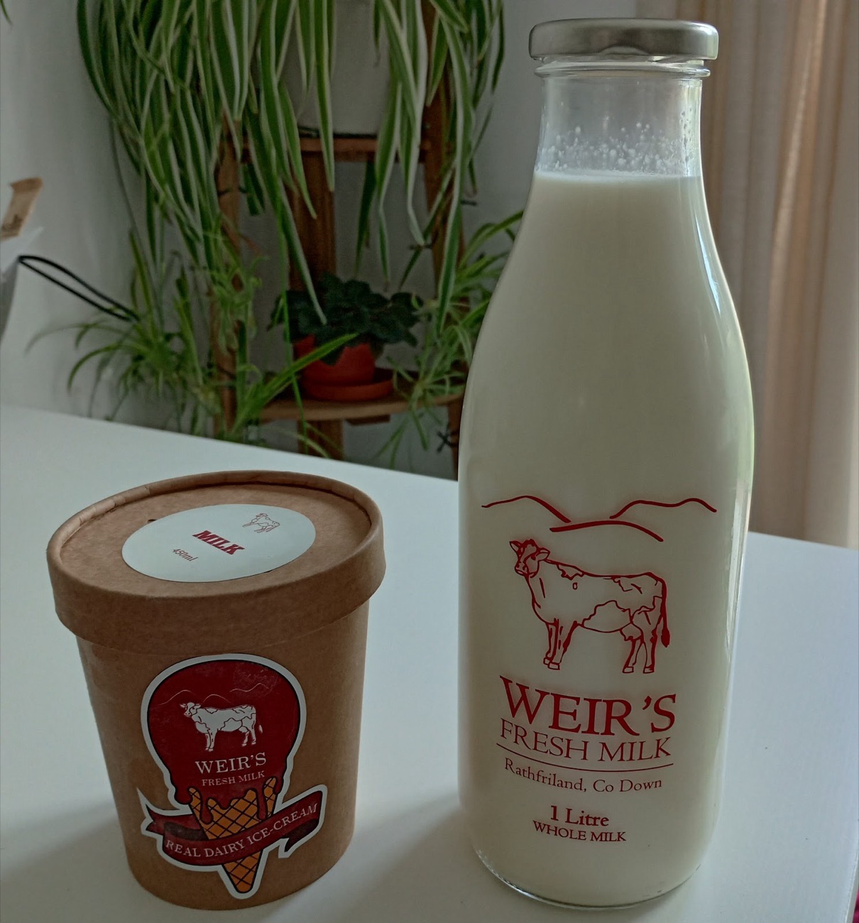 A glass litre bottle of Weir's Fresh Milk beside a tub of their farm ice cream