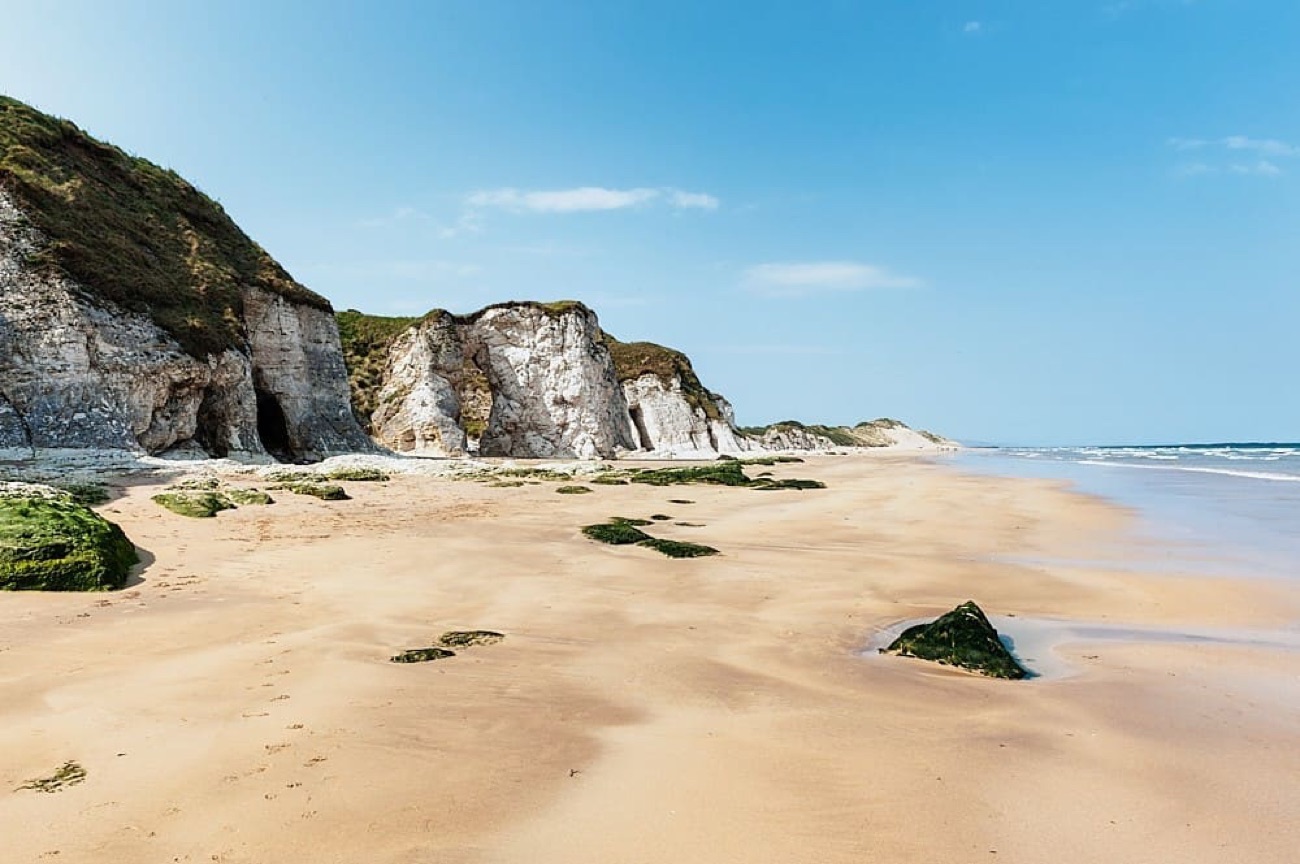 Whiterocks beach at low tide with white limestone cliffs, caves and stacks under a clear blue sky