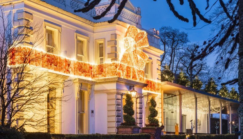 The Galgorm Resort building lit up with warm Christmas lights and a decorated tree on a frosty December evening