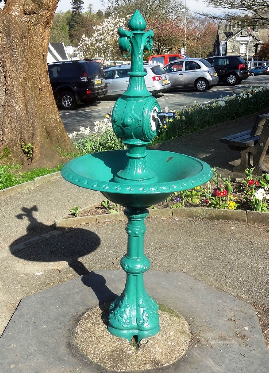 The restored turquoise memorial drinking fountain at Woodvale Park with flower beds behind